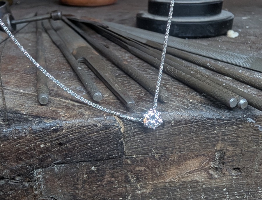 Pendentif solitaire en or blanc posé sur les limes de l'établi